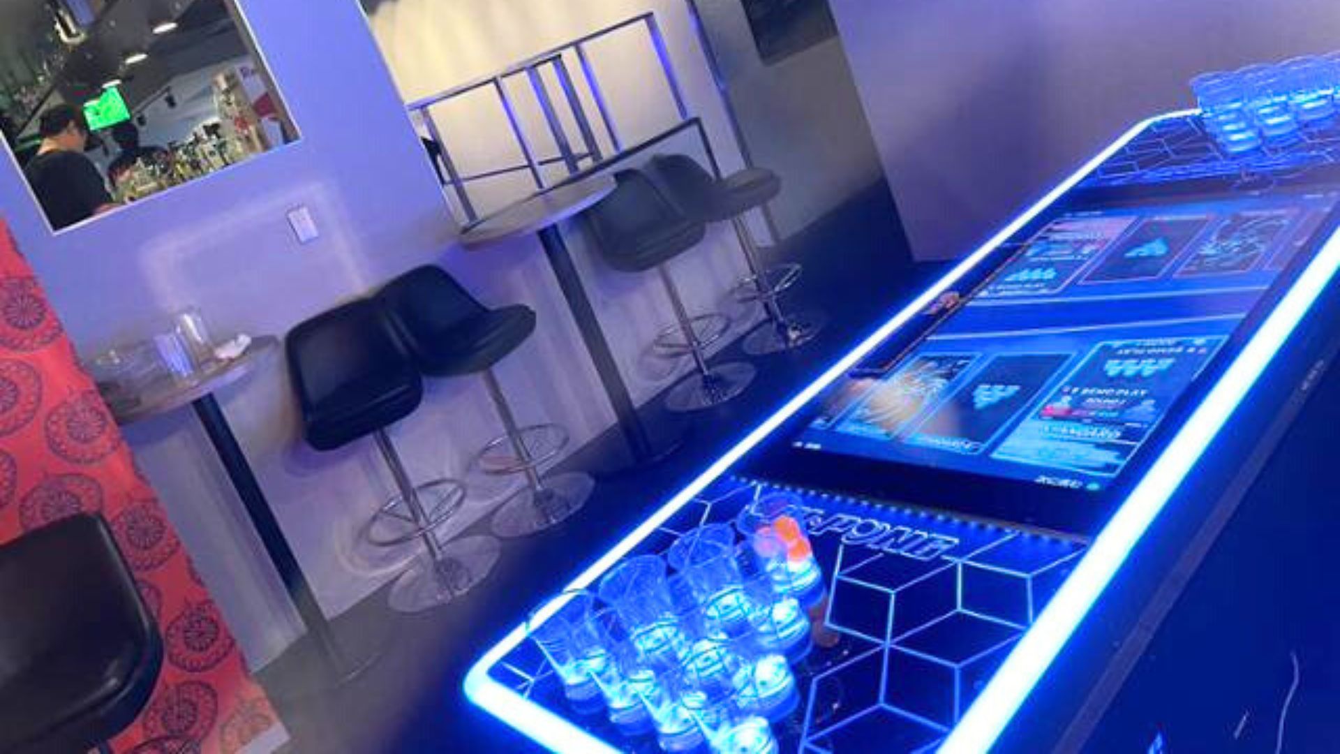 青く光るインタラクティブなテーブルゲーム(おそらくビアポンまたは類似のゲーム)のクローズアップ。テーブルの上には複数のプラスチックカップが置かれている。