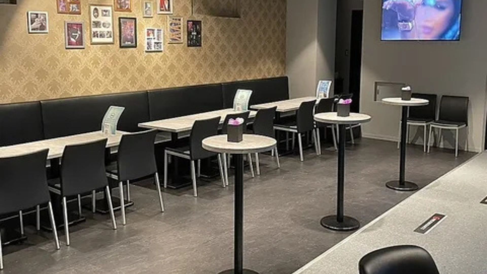 広々としたバーの座席エリア。長いソファ席と、中央には円形の高いテーブルが複数配置されている。壁には額縁に入った写真が飾られている。