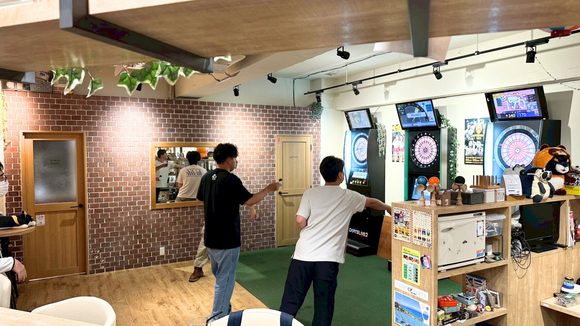 Cafe&bar tricoの店内でダーツを楽しむお客さんたち。奥にはダーツマシンが複数台設置されています。